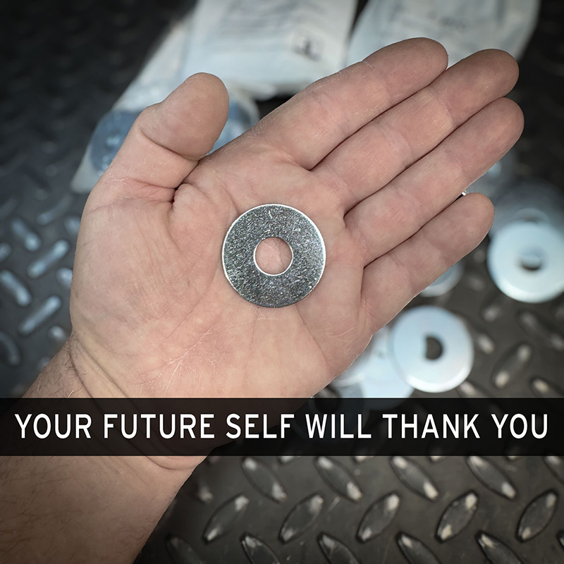 A hand holding a single zinc fender washer from Obtainium Science and Surplus, with more washers visible in the background.